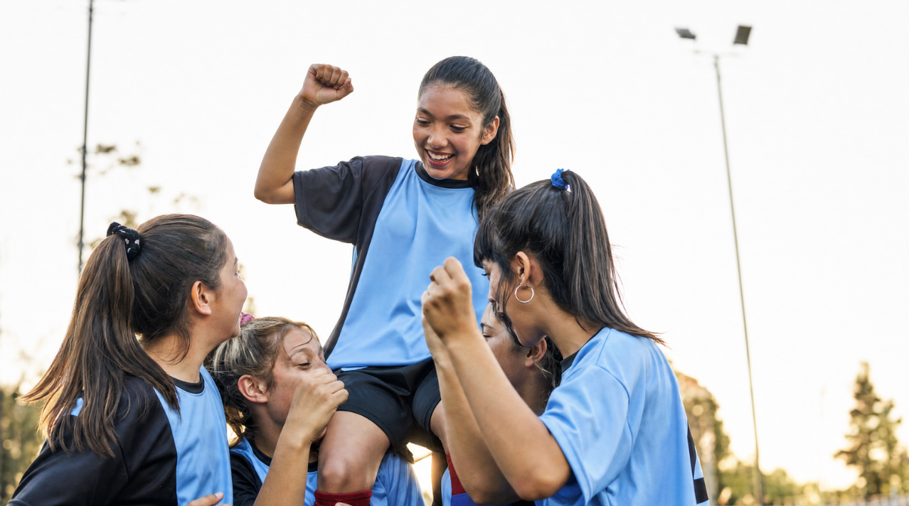 Girls celebrating together on the pitch in team kit