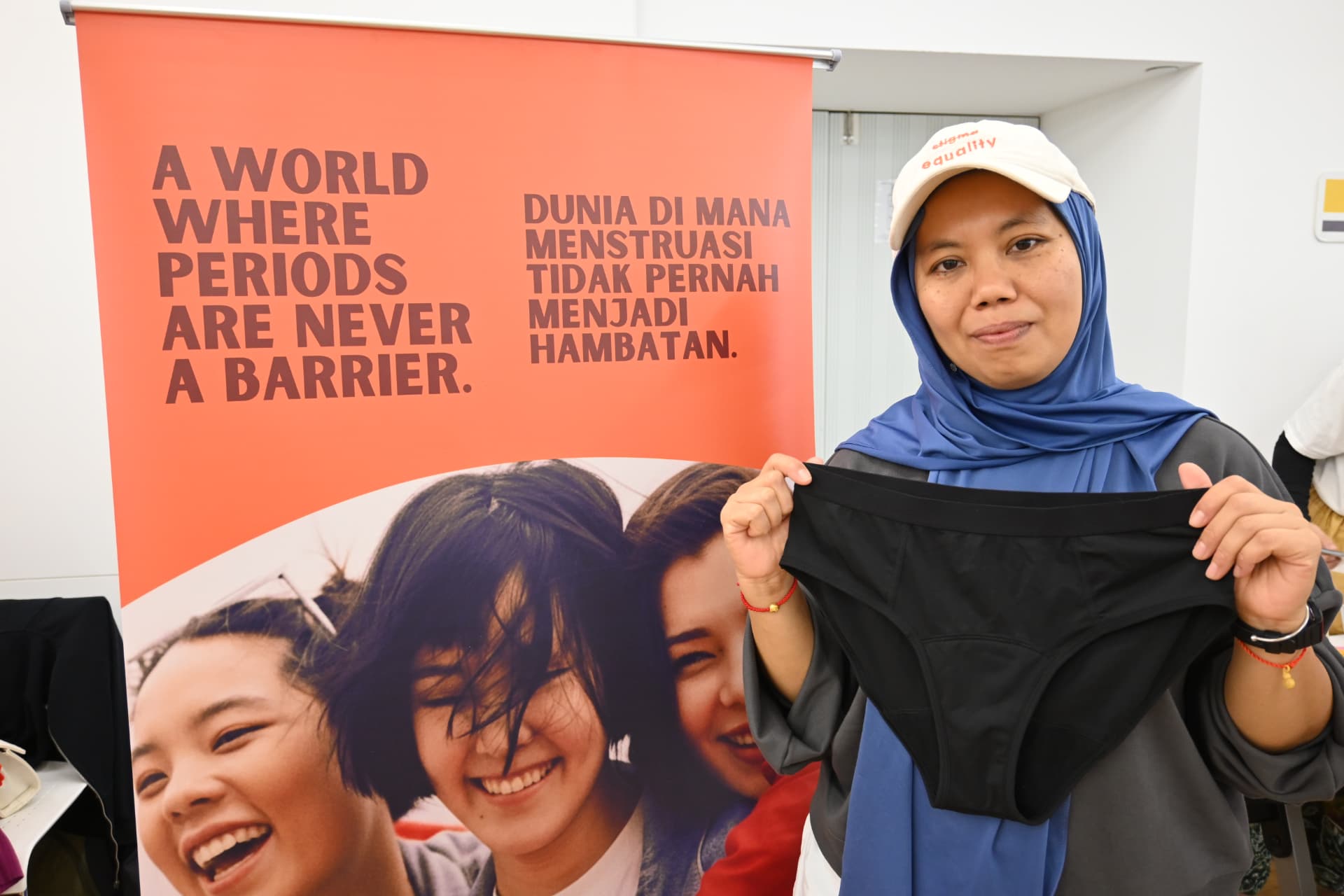 A participant holding reusable period underwear beside a banner reading A world where periods are never a barrier